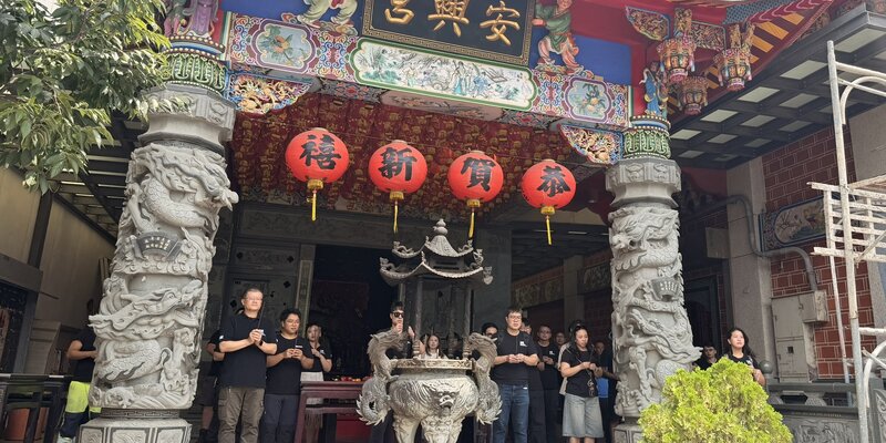 DWT employees holding incense in front of an ornate Chinese temple with red lanterns and dragon pillars. 
