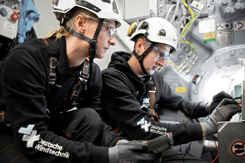 A male and female service technician from Deutsche Windtechnik working on a wind turbine.